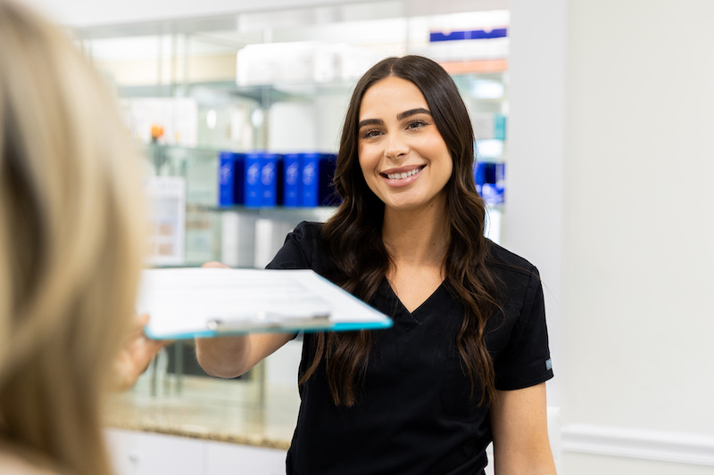 An office assistant is handing a patient prep paperwork for her appointment for facial contouring in Tampa.